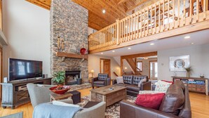A spacious living room with a stone fireplace, wooden ceiling, and a balcony. - Magical Lake Escape w/ Dock Slip & Game Room (Oakland)