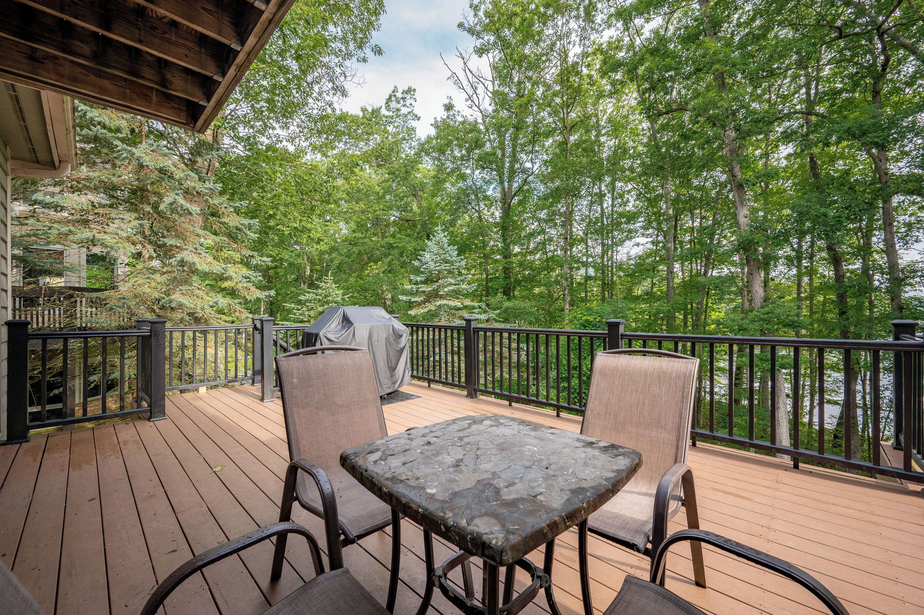 A wooden deck with outdoor furniture, a grill, and a view of a forested area.