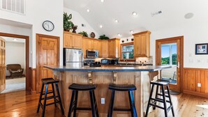 A modern kitchen with wooden cabinets, a stainless steel refrigerator, a microwave, and a large island with bar stools.