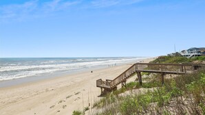 A beach with a wooden boardwalk leading to a building with a balcony overlooking the ocean.