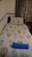Een bed met een cactussen- en plantenprint, een blauwe handdoek en een nachtkastje met een lamp.