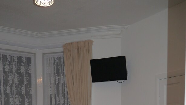 A hotel room with two beds, a TV mounted on the wall, and a window with sheer curtains. - Hornby House Hotel (Blackpool)