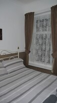 Een slaapkamer met een bed, gordijnen en een raam met bloemrijk gordijn.
