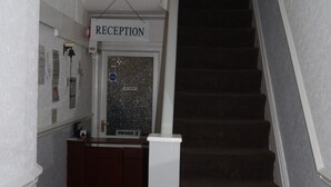 A reception area with a sign, a desk, a trash bin, and a staircase. - Hornby House Hotel (Blackpool)