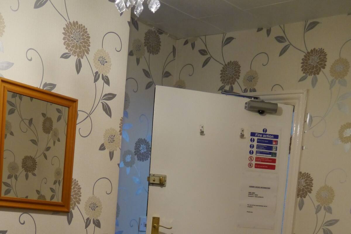 Une chambre d’hôtel équipée d’un lit, d’une commode, d’un miroir et d’une porte sur laquelle est apposé un panneau indiquant les consignes de sécurité en cas d’incendie.