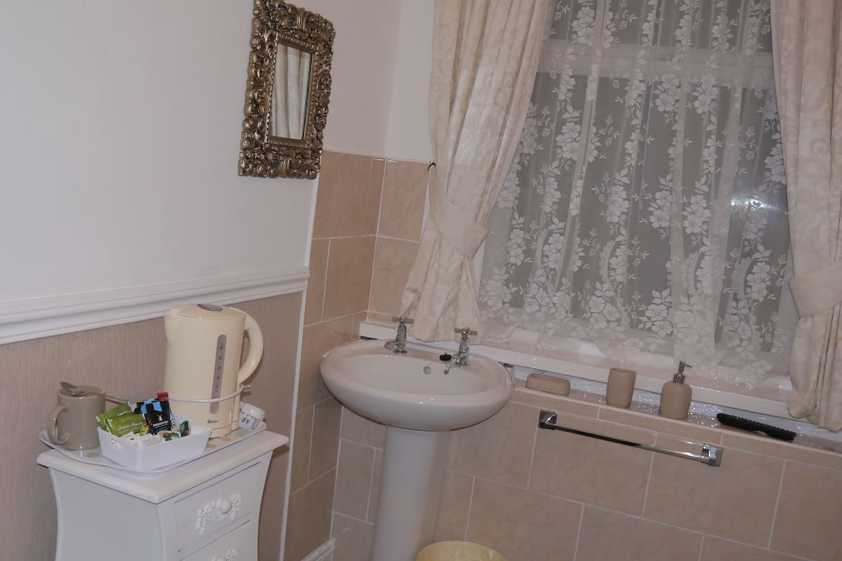 Une salle de bain avec un lavabo, un miroir et une fenêtre agrémentée de rideaux à motifs floraux.