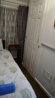 Habitación de hotel con cama, mesita de noche con control remoto, puerta y rejilla en la pared.