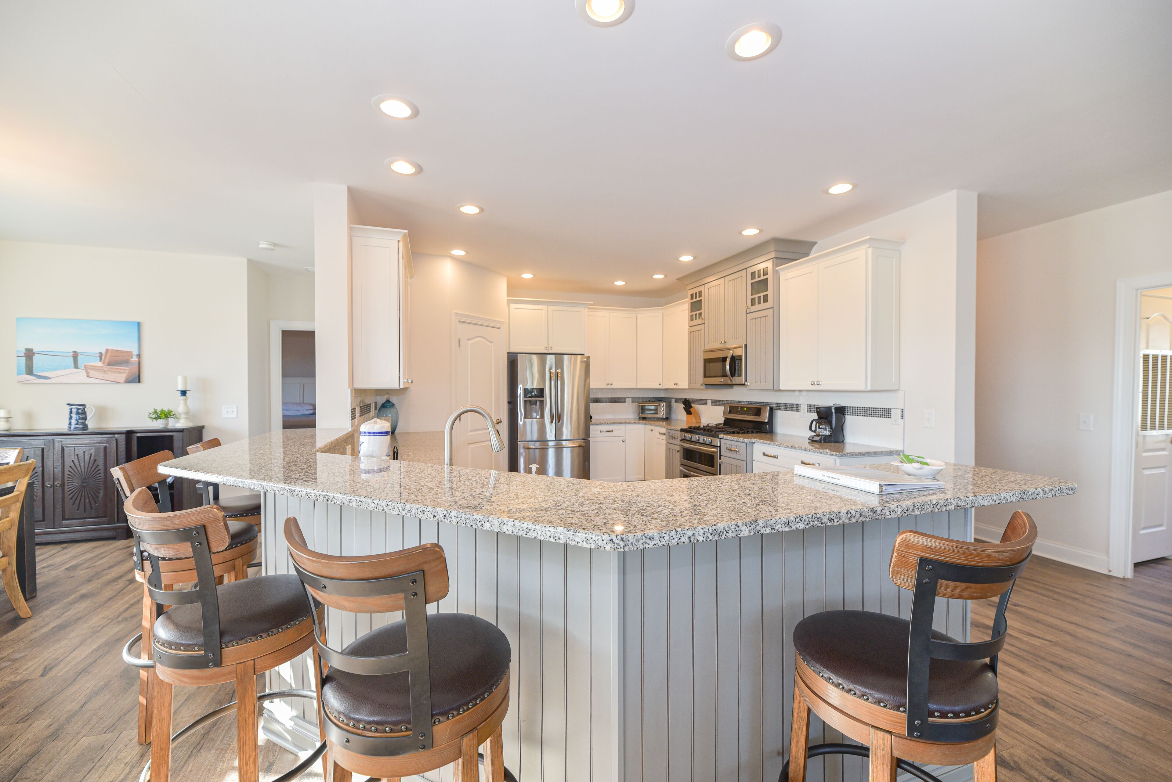 A modern kitchen with a central island, bar stools, stainless steel appliances, and white cabinetry.