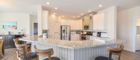 A modern kitchen with a central island, bar stools, stainless steel appliances, and white cabinetry.