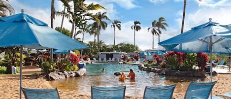 A poolside area with lounge chairs and umbrellas, surrounded by palm trees and tropical plants.