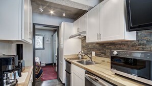 A modern kitchen with white cabinets, stainless steel appliances, a built-in oven, and a large flat-screen TV. - Remodeled Corner Unit with Lots of Light! Walk to Town | PM4A (Breckenridge)