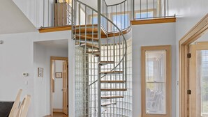 A spacious room with a spiral staircase, wooden flooring, and large windows. - Private pool open and can be heated through Thanksgiving! Pet Friendly! (Corolla)