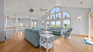 A spacious living area with a high ceiling, large windows, and a view of the outdoors. - Private pool open and can be heated through Thanksgiving! Pet Friendly! (Corolla)