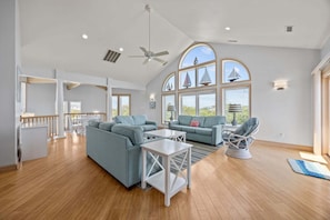 A spacious living area with a high ceiling, large windows, and a view of the outdoors.