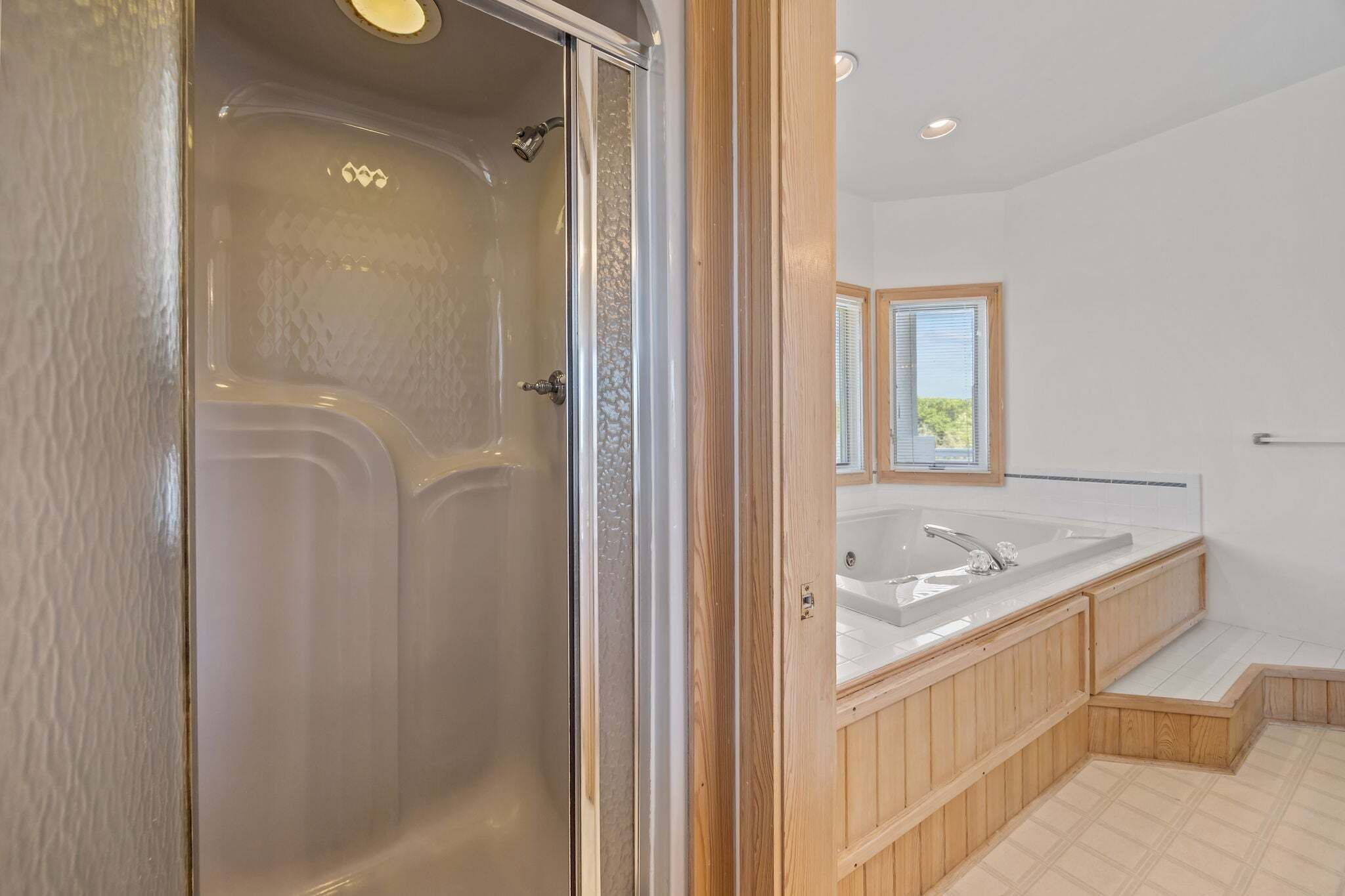 Een moderne badkamer met een douchecabine van glas, een houten wastafelmeubel met een ruime wastafel, en een raam dat voor natuurlijk licht zorgt.