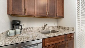 Eine Küche mit Holzausstattung, einer Granit Arbeitsplatte, einer Edelstahl-Spüle und einer Kaffeemaschine.