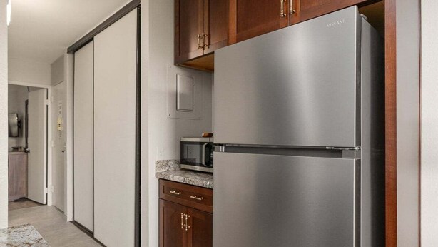 A kitchen with a stainless steel refrigerator, wooden cabinets, a microwave, and a granite countertop.