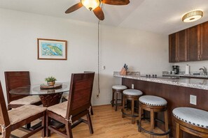 Un coin repas avec une table ronde en verre, des chaises en bois et un ventilateur de plafond.
