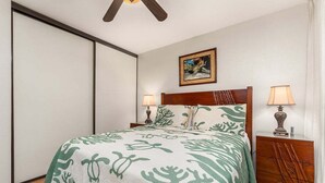 A bedroom with a bed, two bedside tables, a ceiling fan, a painting on the wall, and a sliding door.