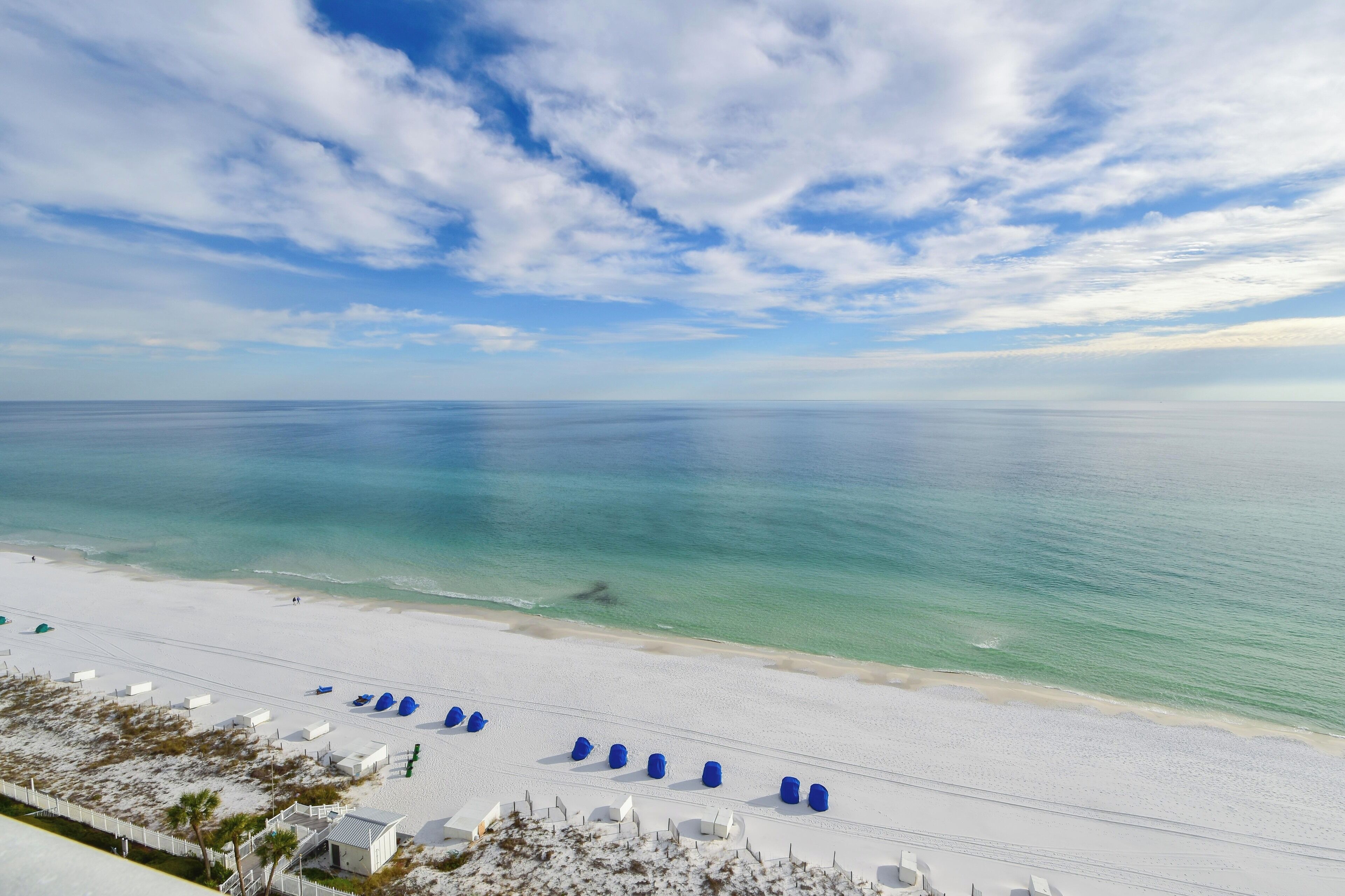 A beach with white sand, clear turquoise water, and a row of blue beach chairs.