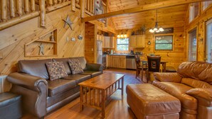 A log cabin interior with a living room featuring a brown leather sofa, a wooden coffee table, and a fireplace. - Secluded | Pet Friendly | Pool Table | Arcade | Hot Tub | WiFi (SEVIERVILLE)