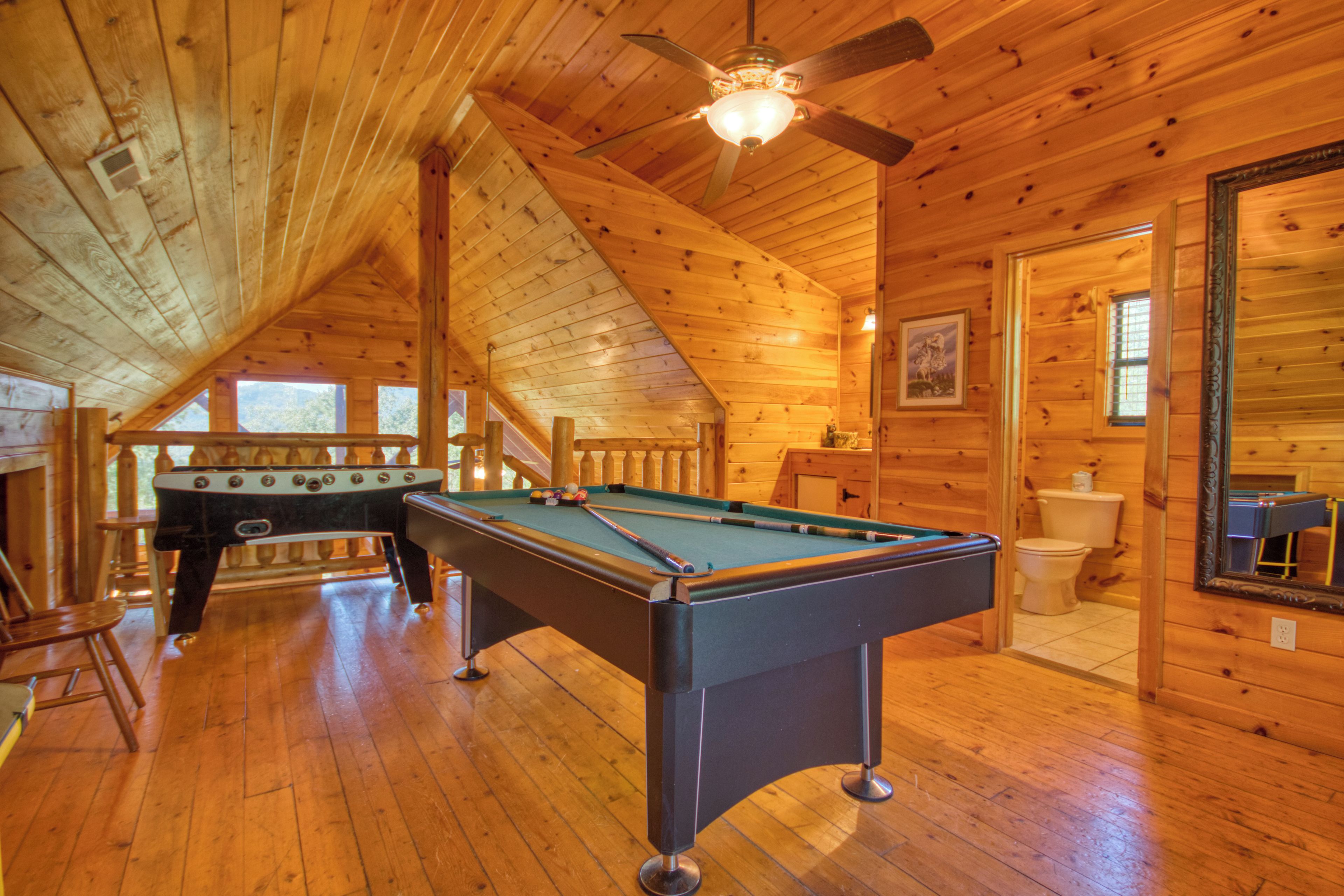 Un intérieur en bois avec une table de billard, une table de baby-foot et un ventilateur de plafond.