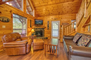 A log cabin interior with a fireplace, leather furniture, and a television. - Secluded | Pet Friendly | Pool Table | Arcade | Hot Tub | WiFi (SEVIERVILLE)