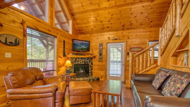 A log cabin interior with a fireplace, leather furniture, and a television. - Secluded | Pet Friendly | Pool Table | Arcade | Hot Tub | WiFi (SEVIERVILLE)