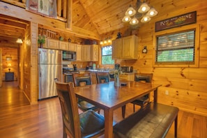 A wooden cabin interior with a dining area, kitchen, and a clock on the wall. - Secluded | Pet Friendly | Pool Table | Arcade | Hot Tub | WiFi (SEVIERVILLE)