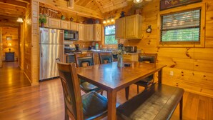 A wooden cabin interior with a dining area, kitchen, and a clock on the wall. - Secluded | Pet Friendly | Pool Table | Arcade | Hot Tub | WiFi (SEVIERVILLE)