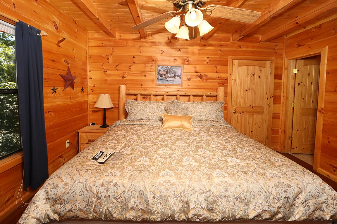 Ein Schlafzimmer in einer Holzhütte mit einem Bett, einem Nachttisch, einer Lampe und einem Deckenventilator.