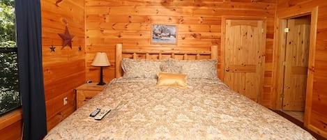 Ein Schlafzimmer in einer Holzhütte mit einem Bett, einem Nachttisch, einer Lampe und einem Deckenventilator.