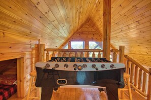 A wooden cabin with a loft bed, a wooden table, and a window with a view of trees. - Secluded | Pet Friendly | Pool Table | Arcade | Hot Tub | WiFi (SEVIERVILLE)