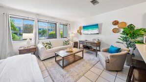 Ein modernes Wohnzimmer mit Sofa, Sessel, Couchtisch und Fernseher an der Wand.
