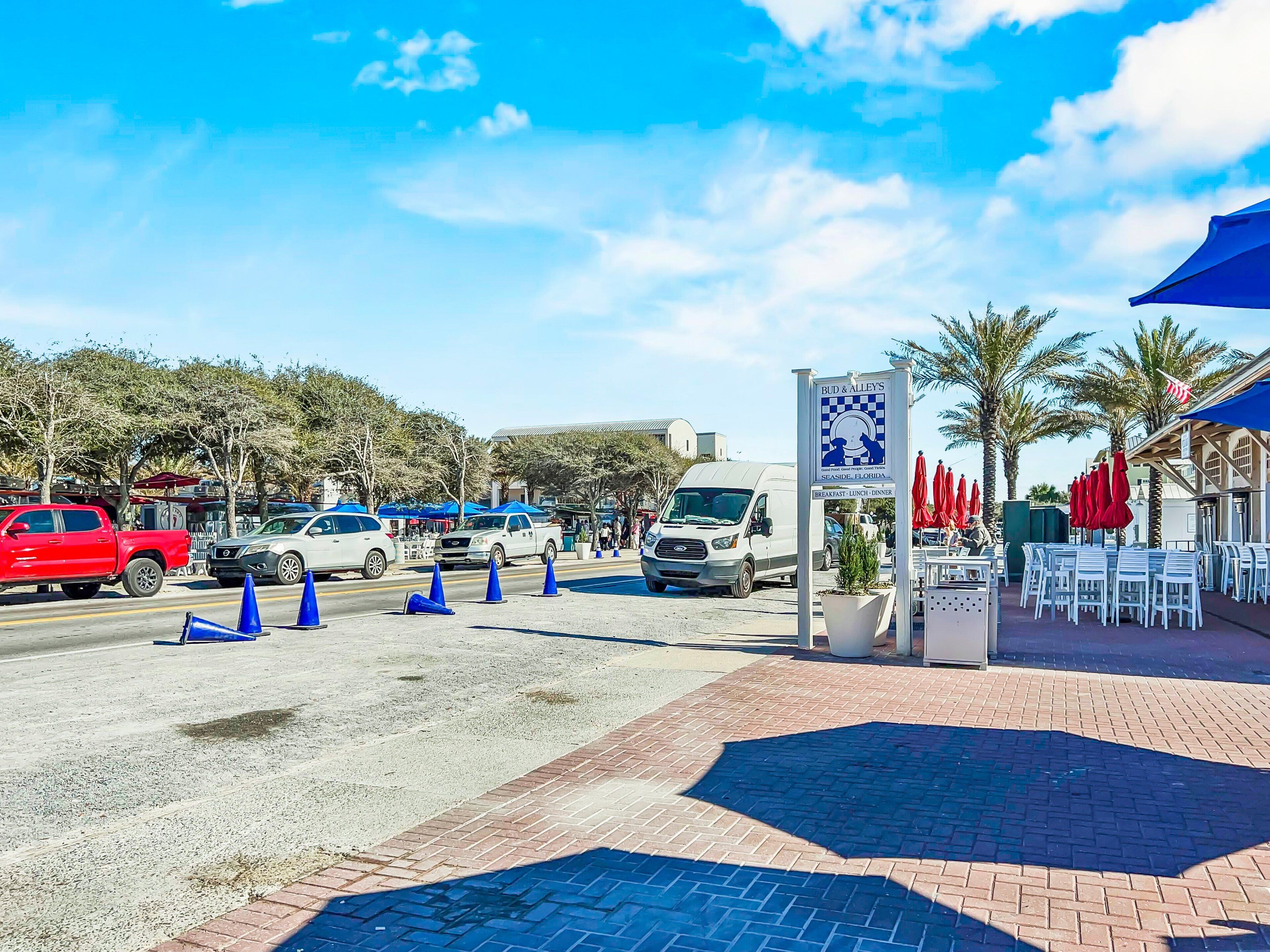 A parking area with a Bud & Alley's sign, a white van, and several cars.