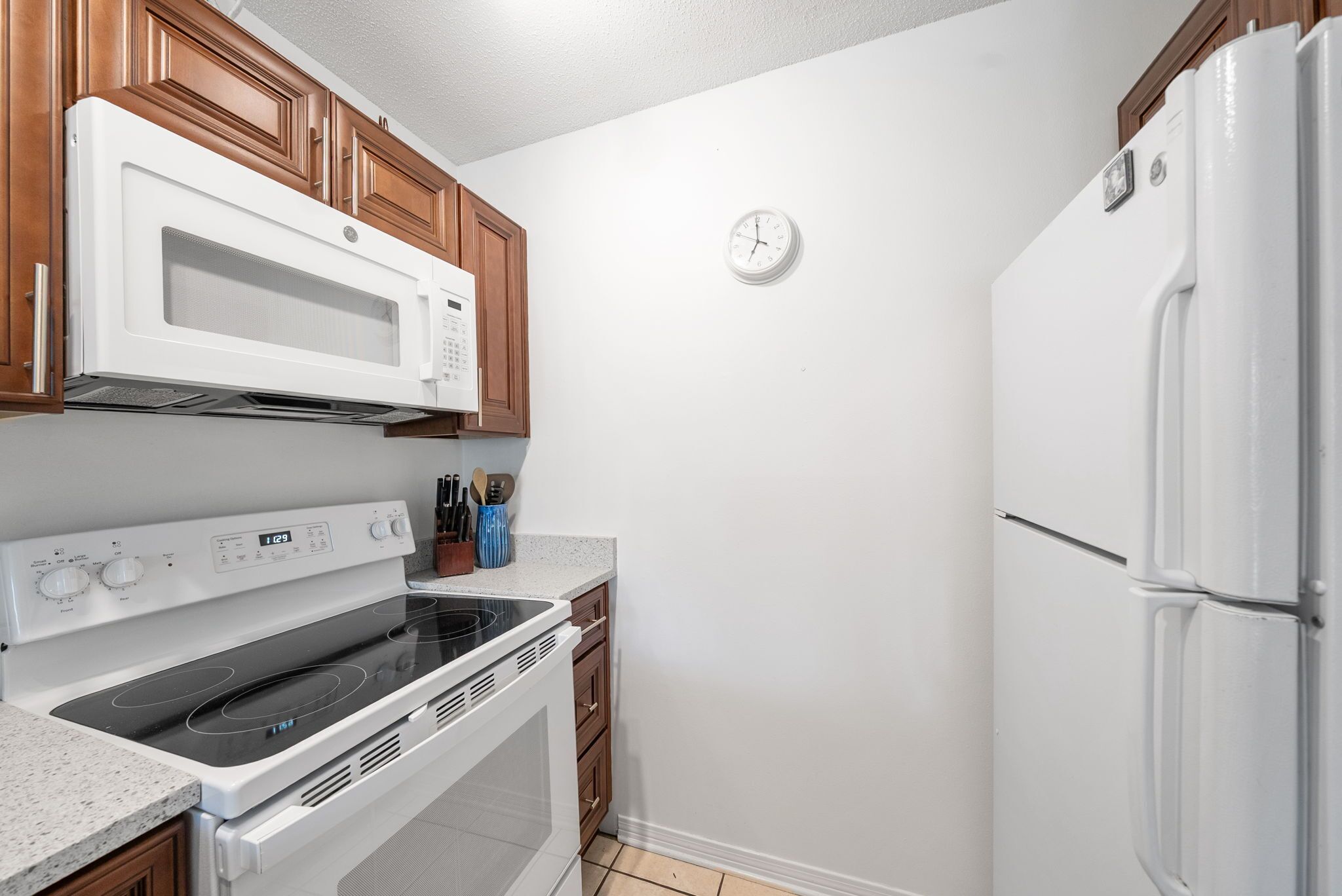 A kitchen with white appliances, wooden cabinets, a microwave, stove, and a refrigerator.