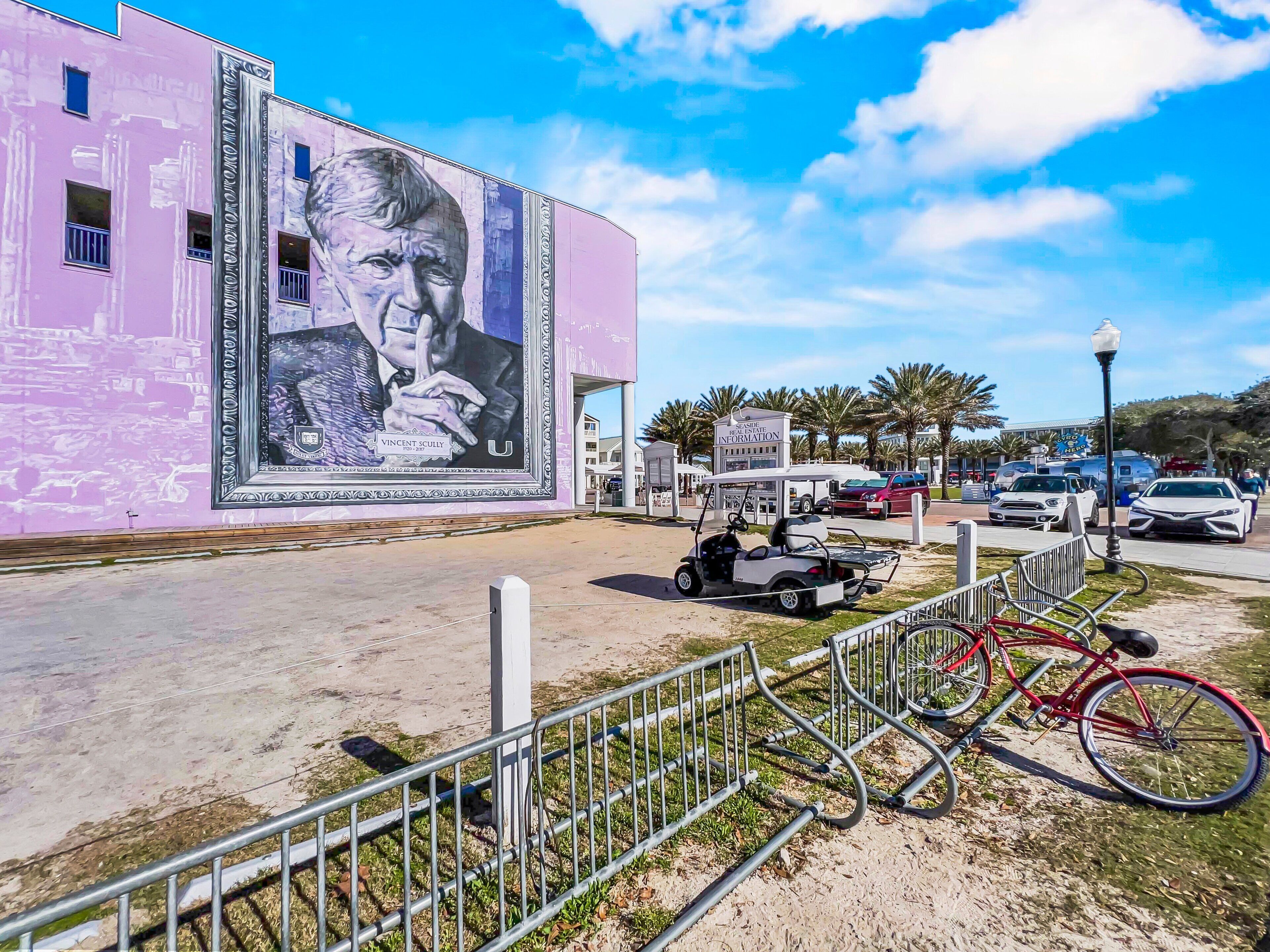 A building with a large mural, a golf cart, and a bicycle.
