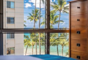 A room with a view of palm trees and the ocean through a window. - Updated Oceanview Oasis w/AC - Kamaole Nalu 502: Your Ultimate Maui Retreat! (Kihei)