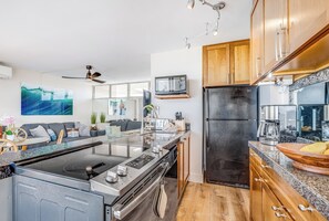 A modern kitchen with a central island, wooden cabinets, and a black refrigerator. - Updated Oceanview Oasis w/AC - Kamaole Nalu 502: Your Ultimate Maui Retreat! (Kihei)