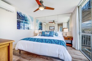 Una camera d'albergo con un letto grande, ventilatori a soffitto, una scrivania in legno e una grande finestra con tende.