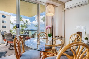 A glass-top dining table with wicker chairs, a potted plant, and a view of palm trees and the ocean. - Updated Oceanview Oasis w/AC - Kamaole Nalu 502: Your Ultimate Maui Retreat! (Kihei)