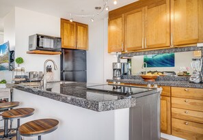 Eine moderne Küche mit Granit-Arbeitsplatten, Holzschränken, einem Edelstahl-Kühlschrank und einer eingebauten Mikrowelle.