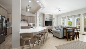A modern kitchen with a central island, bar stools, a flat-screen TV, and a dining area with a table and chairs.