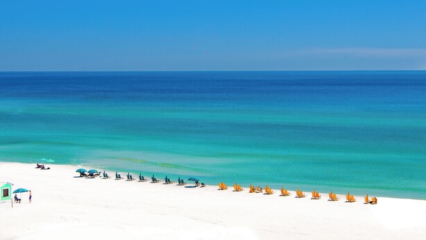 A beach with rows of sun loungers and umbrellas, a lifeguard tower, and a clear view of the ocean.