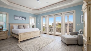 A bedroom with a large bed, a chair, a dresser, and a balcony with a view of houses.