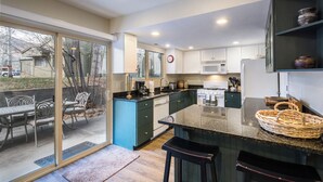 Une cuisine moderne dotée d’un grand îlot central, de portes-fenêtres coulissantes donnant sur un patio et offrant une vue sur le jardin arrière.