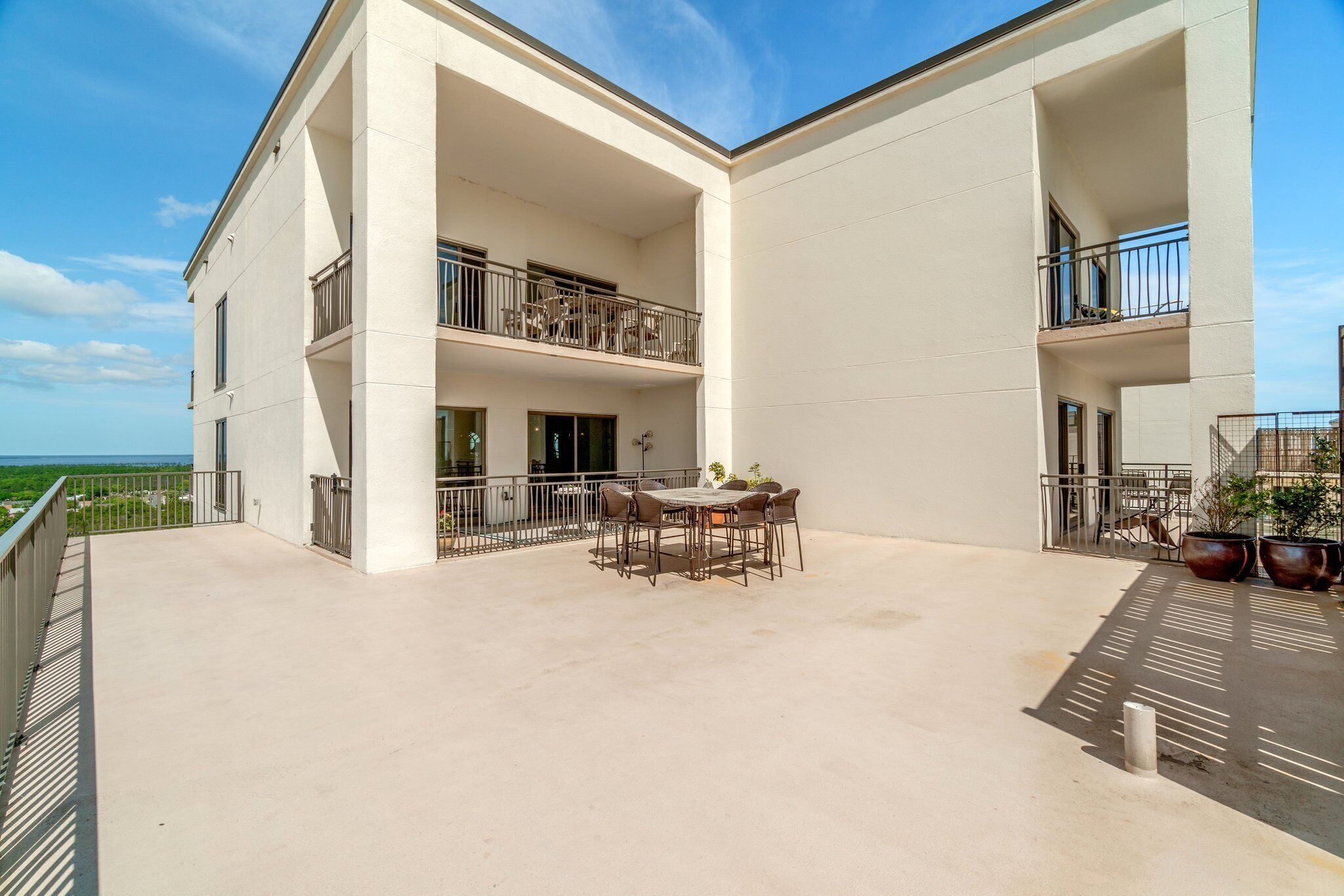 A modern building with a flat roof and two balconies, one with a table and chairs.