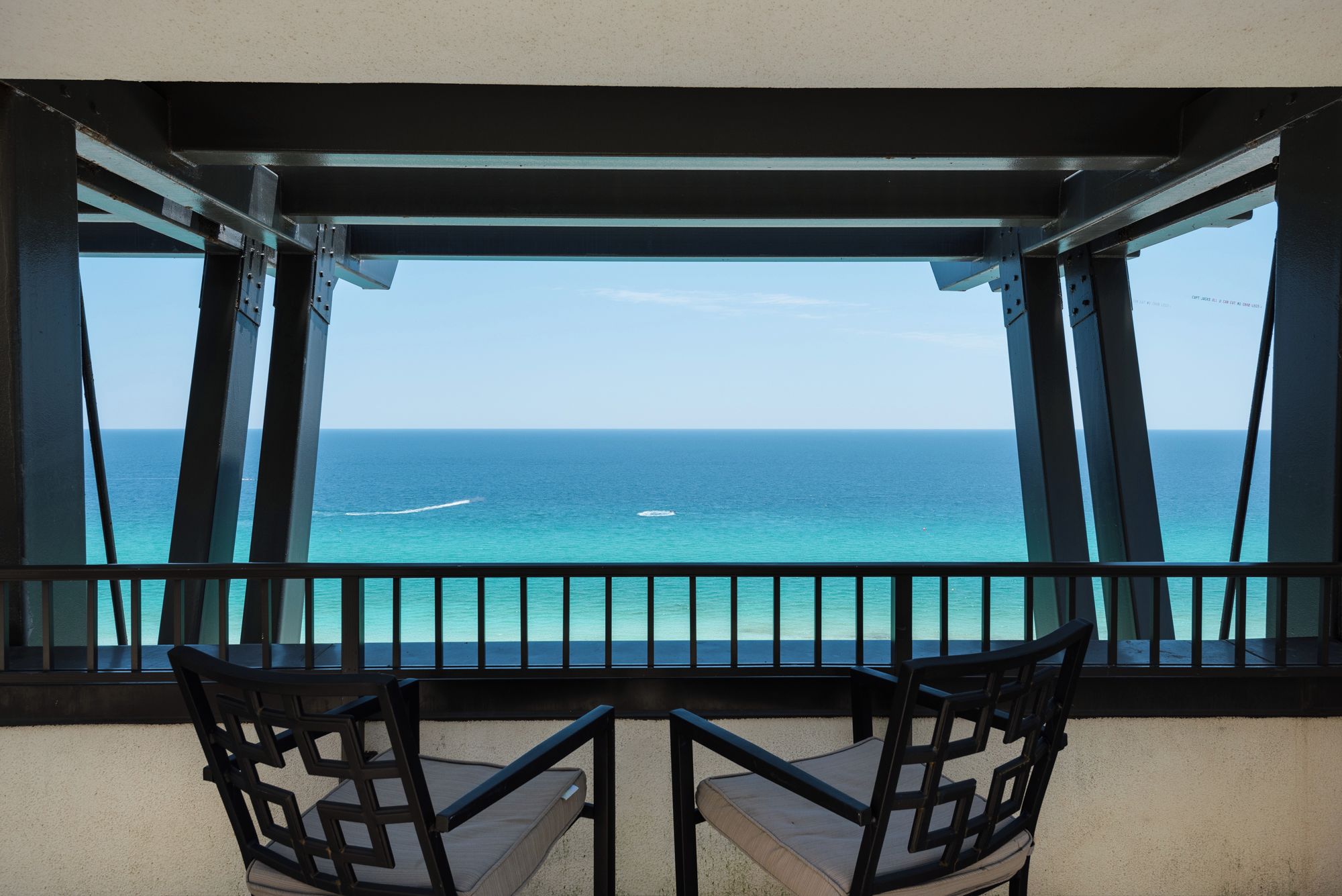 A balcony with two chairs facing a view of the ocean.