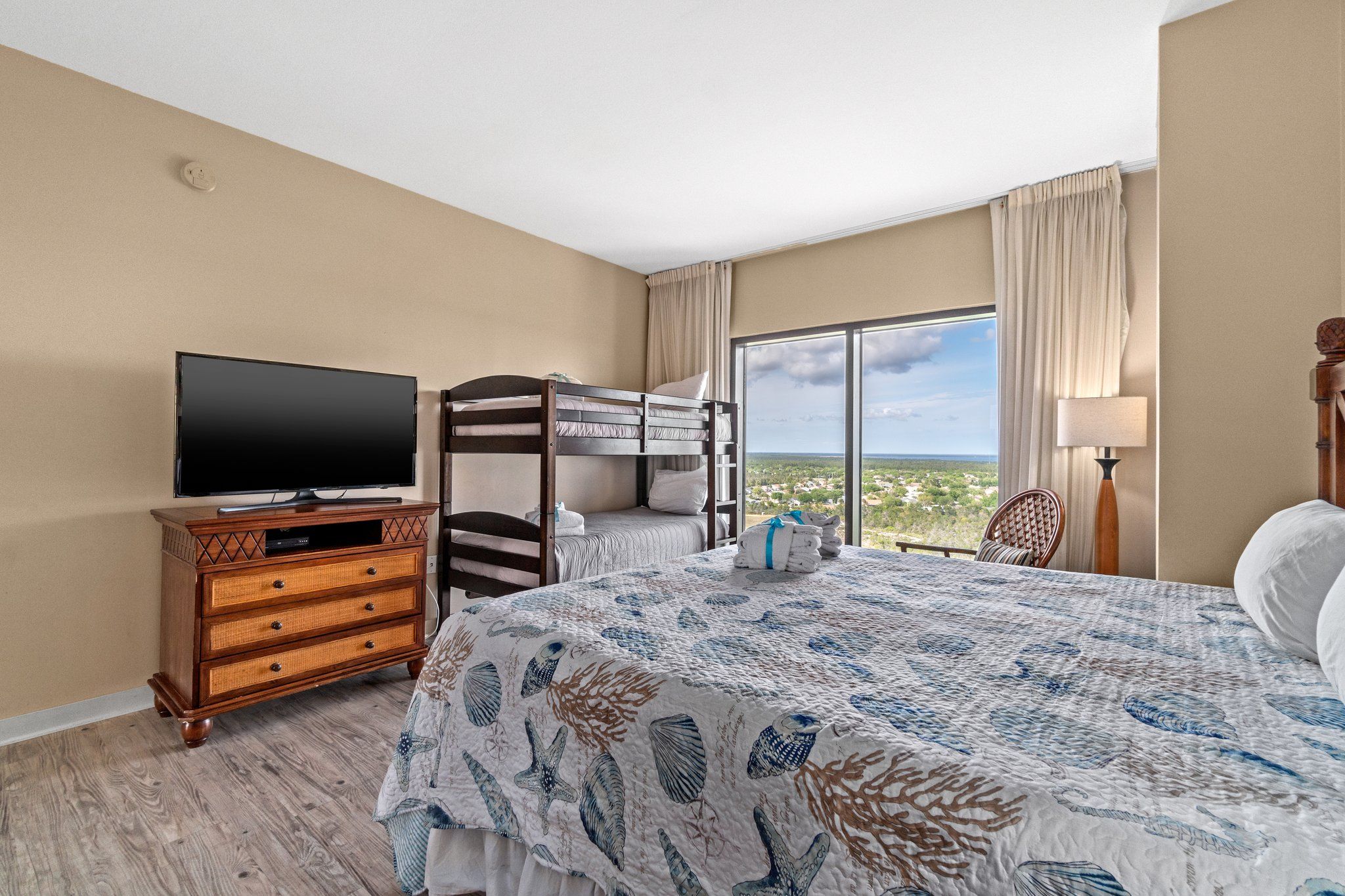 Habitación de hotel con literas, un televisor de pantalla plana, cómoda de madera y un ventanal con vistas al paisaje.
