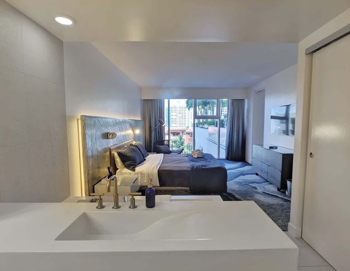 Ein modernes Hotelzimmer mit einer großen, weißen Badewanne, einem Bett mit Kopfteil, einem Schminktisch und einem an der Wand befestigten Fernseher.